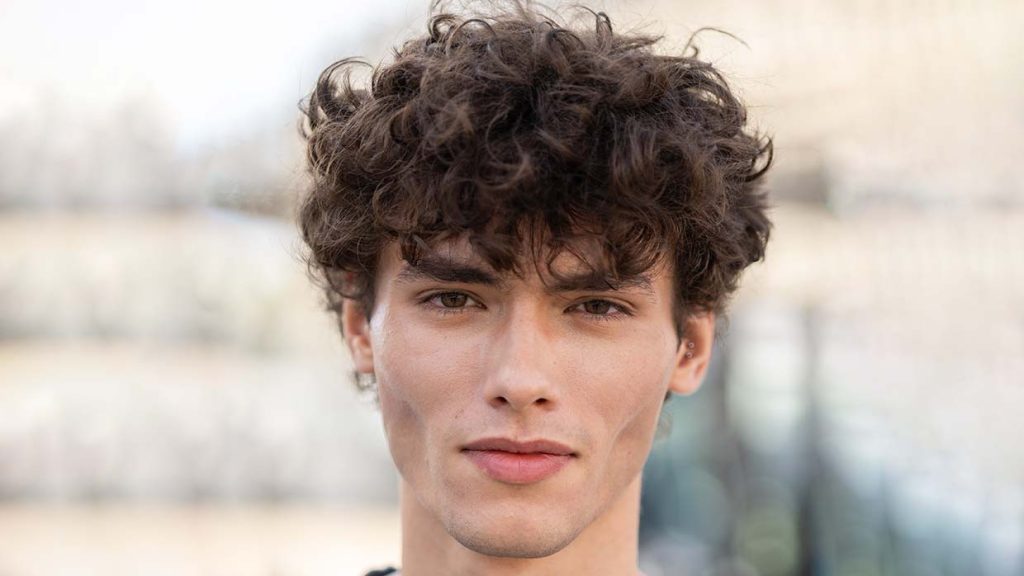 Krullende herenkapsels zomer 2027: dit zijn de trends. Krullend herenkapsel met volumineuze bovenkant bij Loewe tijdens de Paris Fashion Week. Foto ADVERSUS